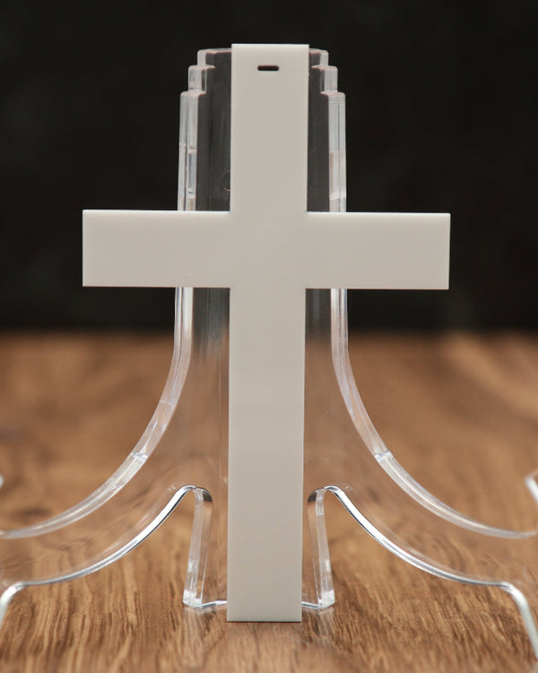 A white cross-shaped acrylic Christmas ornament, displayed on a wooden surface against a dark background.
