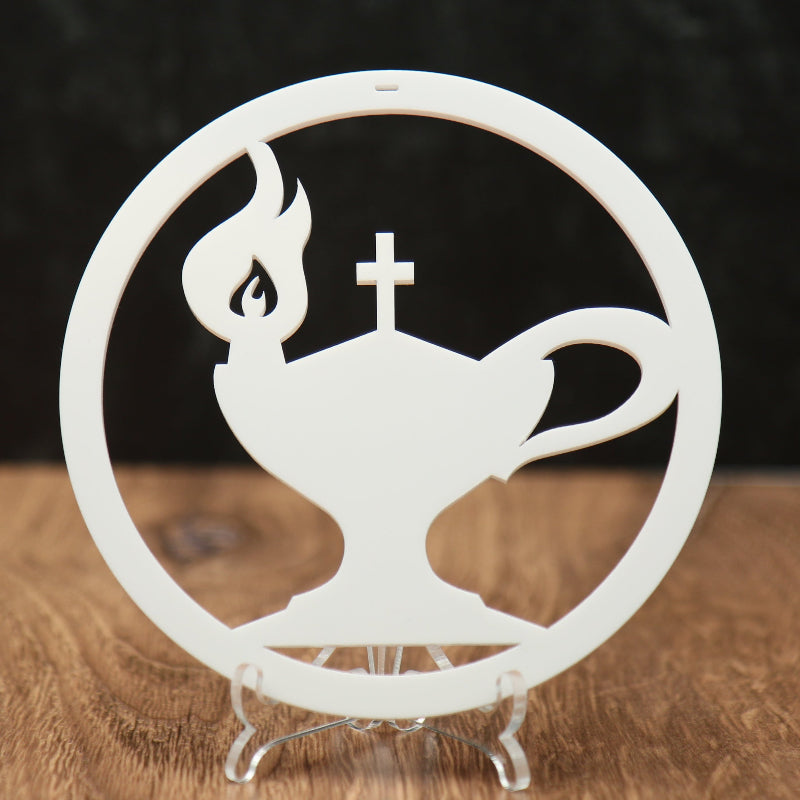 A white circular acrylic Christmas ornament featuring a stylized oil lamp with a cross on top, displayed on a clear acrylic stand on a wooden surface against a dark textured background.