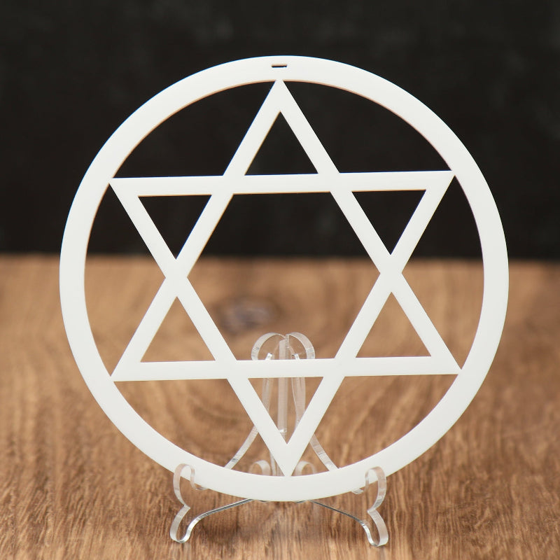 A white circular Star of David Christmas ornament  cutout displayed on a small clear stand, set on a wooden surface against a dark textured background.