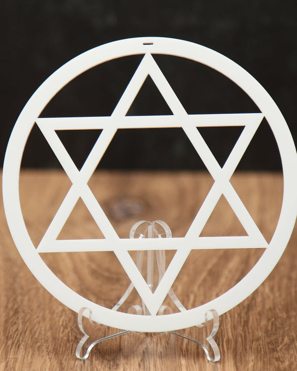 A white circular Star of David Christmas ornament  cutout displayed on a small clear stand, set on a wooden surface against a dark textured background.