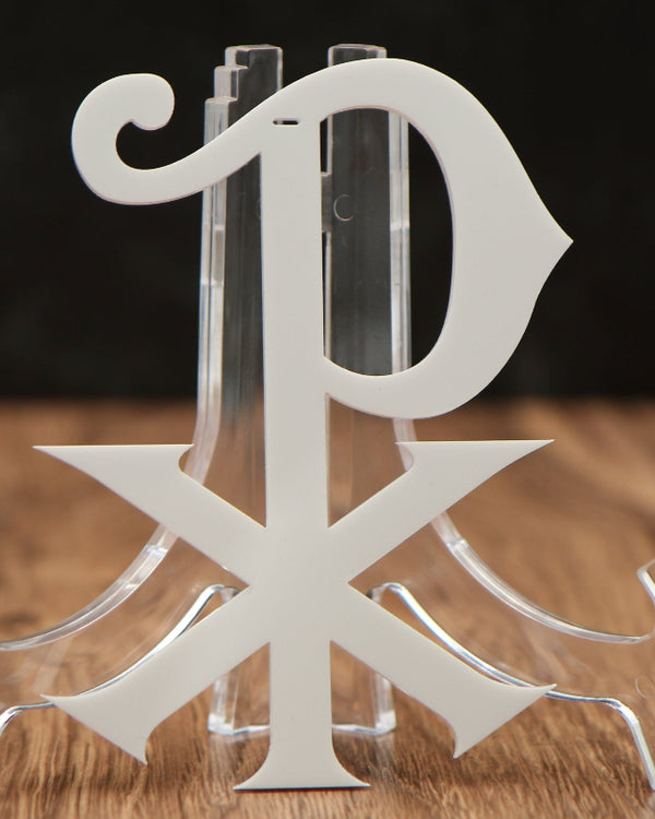 A clear acrylic monogram stand featuring the letters 'P' and 'X' in a monogrammed design, displayed on a wooden surface with a dark background.