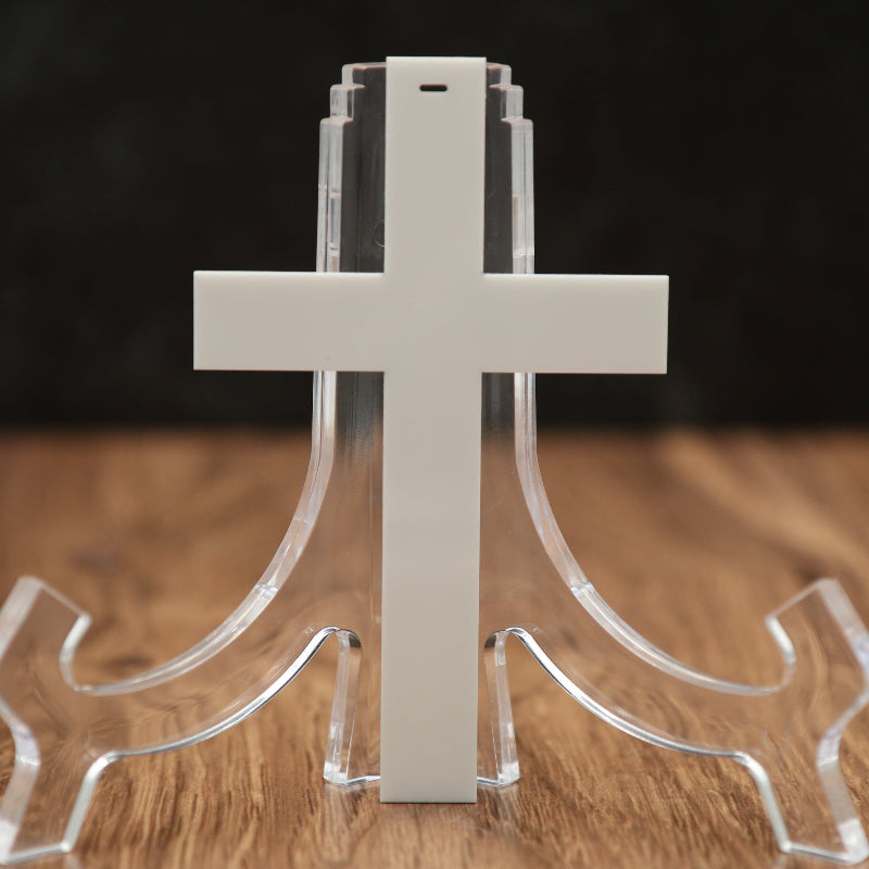A white cross-shaped acrylic Christmas ornament, displayed on a wooden surface against a dark background.