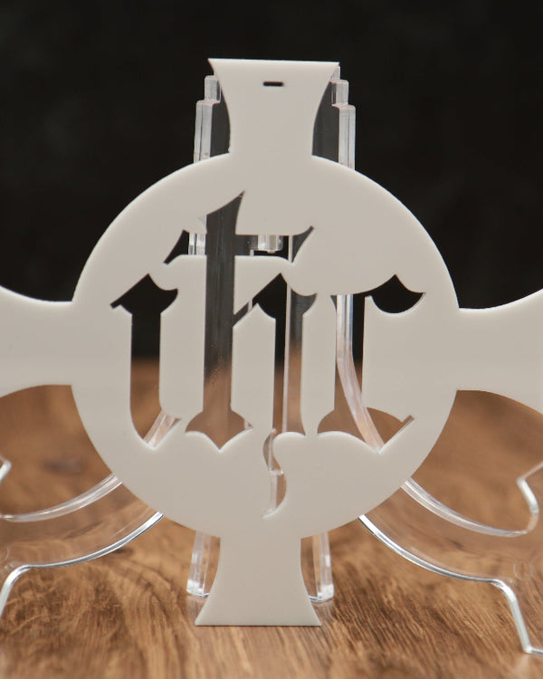 A clear acrylic decorative stand featuring a central cutout design with the letters 'I', 'H', and 'C' arranged in a circular motif, displayed on a wooden surface against a dark background.