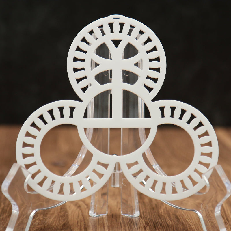 A white circular acrylic stand with three interlocking ring-like discs and clear acrylic legs, photographed on a wooden surface against a dark background.