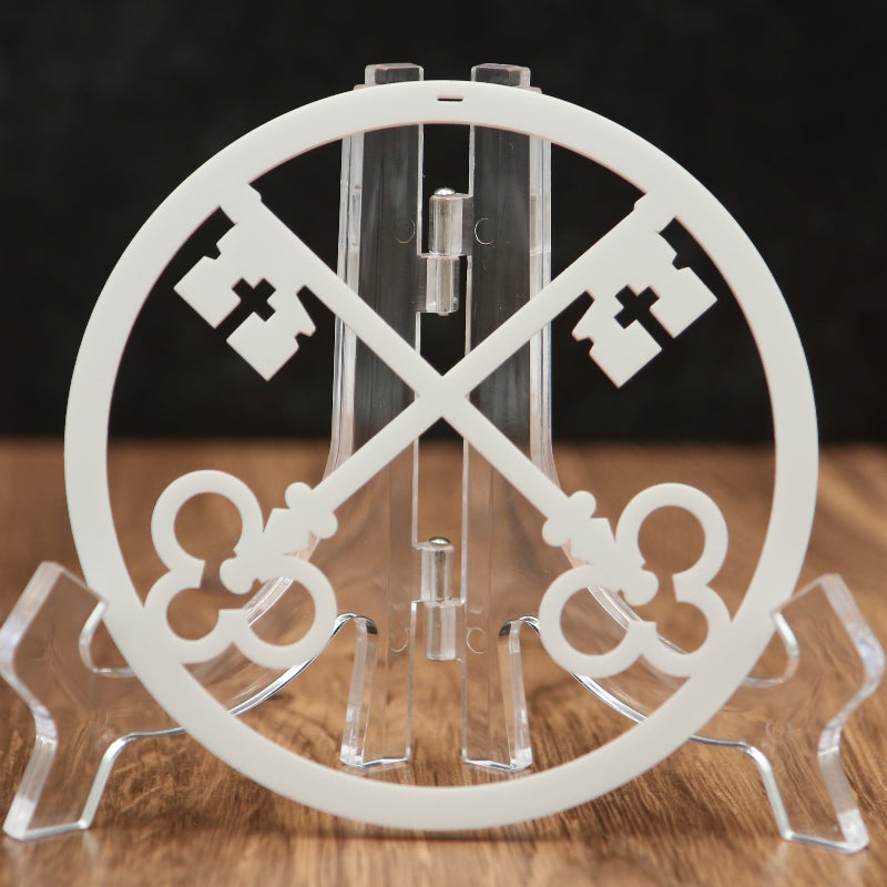 A white circular acrylic stand featuring two crossed decorative keys, displayed on a clear acrylic easel over a wooden surface against a dark background.