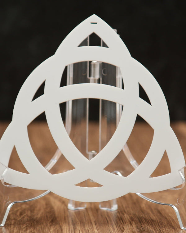 A white triangular interlocking rings cutout acrylic Christmas ornament displayed on a clear acrylic stand, set on a wooden surface against a dark background.