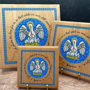 Three rectangular wooden plaques with rounded corners, each featuring a blue mosaic-style pelican design, decorative border, and scripture text, displayed on a tabletop against a dark textured background.