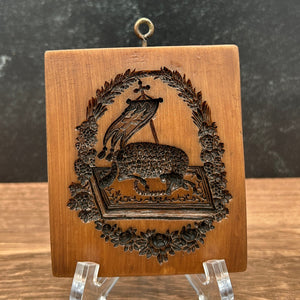 A rectangular wooden box with a carved decorative crest featuring a bird and floral border, displayed on clear acrylic stands against a split dark gray and brown wood background.