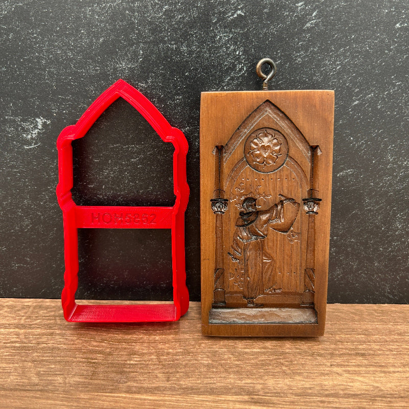 A brown carved cookie cutter showing Dr Martin Luther  in a doorway, placed above a red cookie cutter or mold on a split dark gray and wood surface.