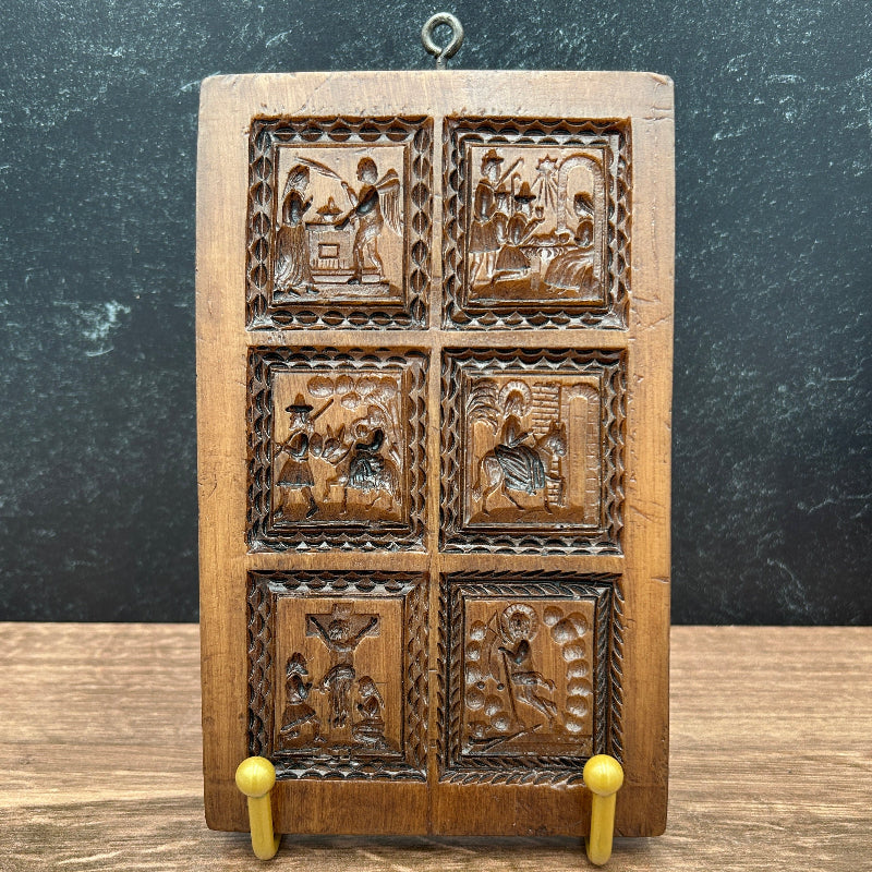 A rectangular cookie mold with six carved square panels, shown against a split dark gray and wood-grain background.